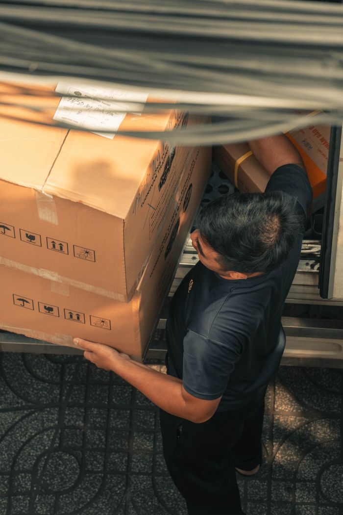 services-01 Delivery worker loading boxes from truck on urban city street during daytime.