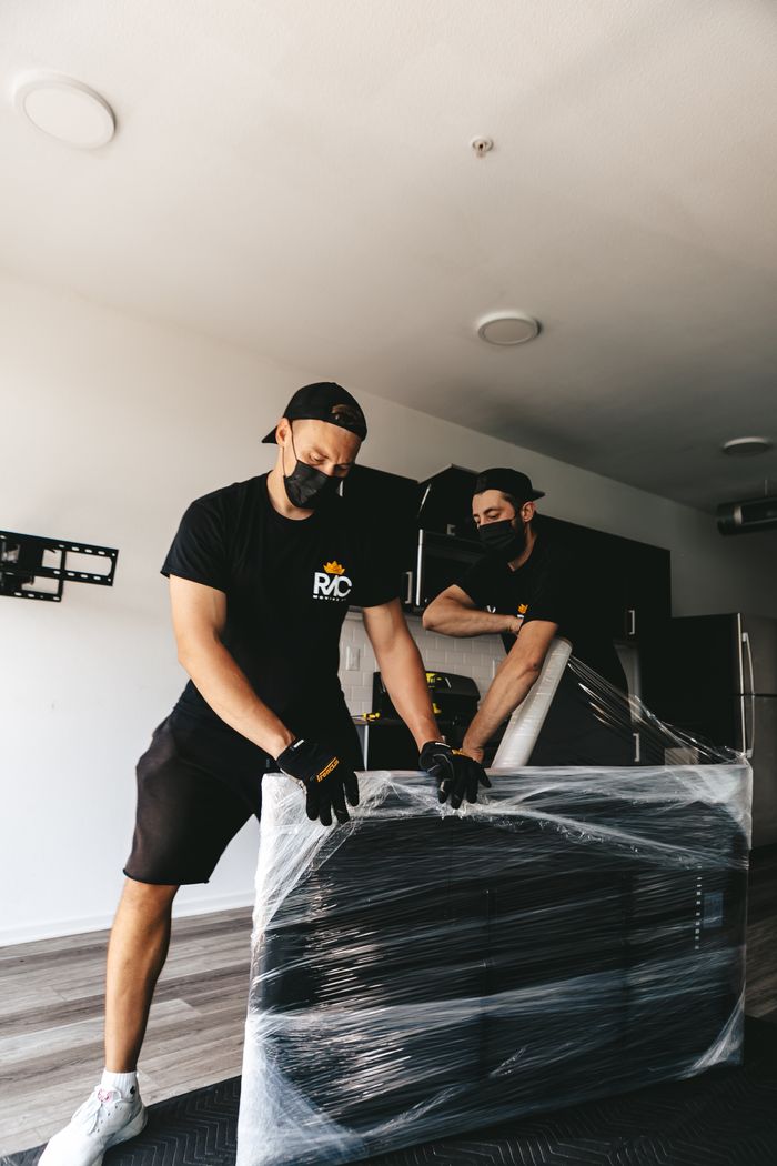 services-02 Two masked men moving a securely wrapped item in a modern room.