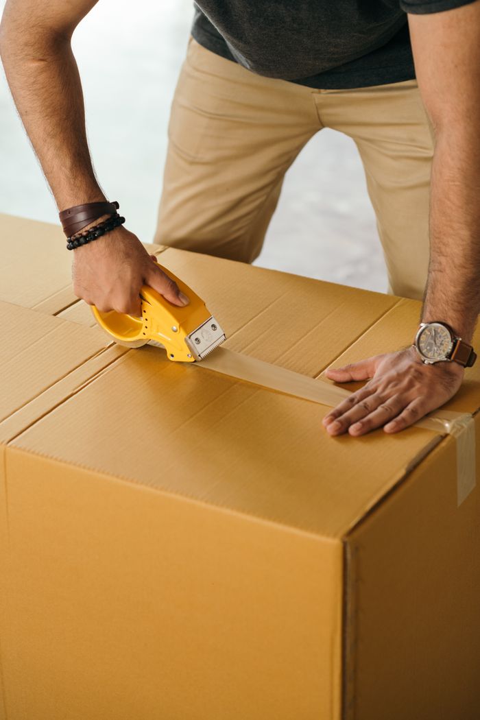 services-02 Unrecognizable man sealing box with duck tape while preparing for moving out
