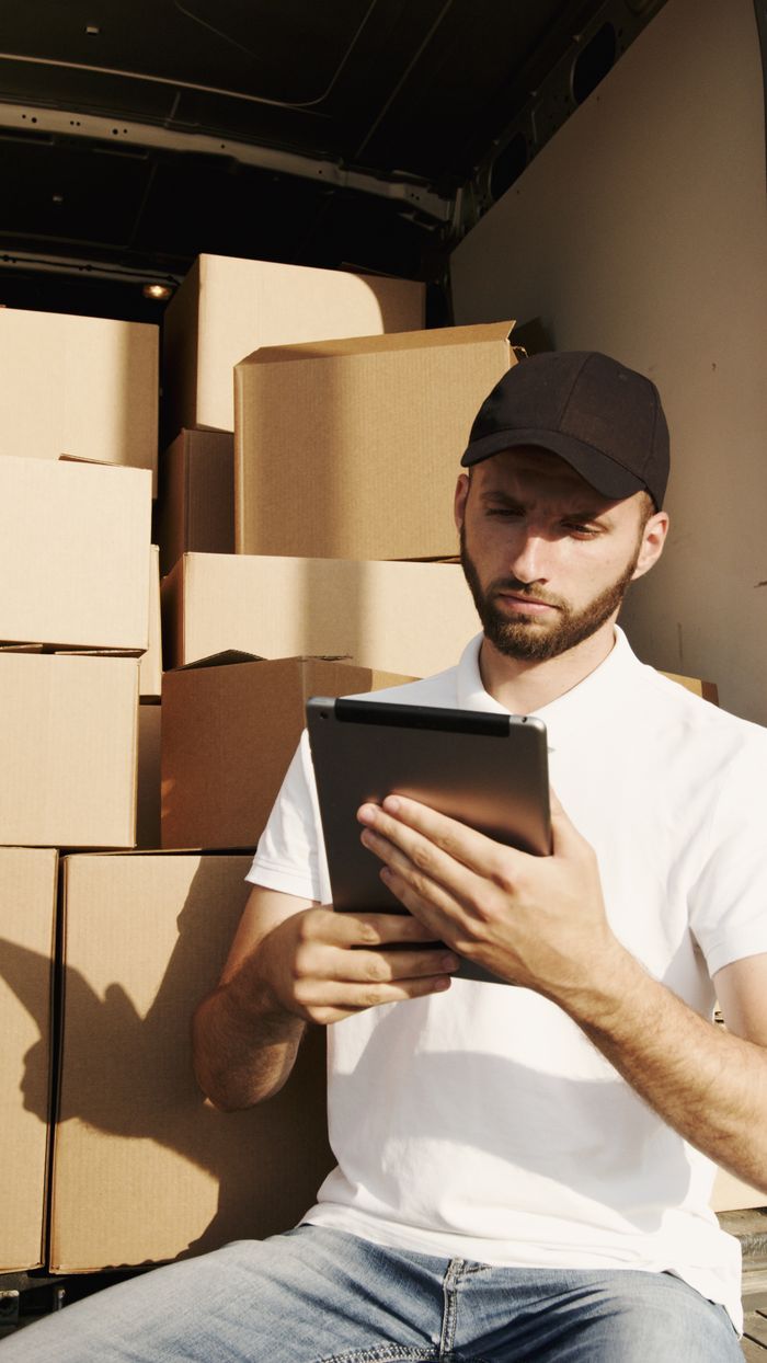 contact-img Deliveryman using a digital tablet to manage packages in a van. Efficient courier service with boxes.