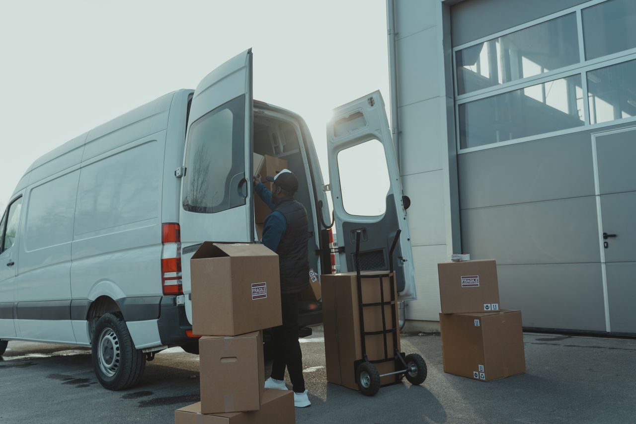 why-choose-us Courier loading cardboard boxes into a delivery van outside a warehouse.